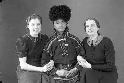 Porträtt av en herre i samedräkt och två damer. Ateljefoto.