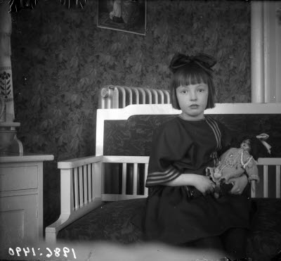 En flicka med docka. Hemmiljö; vardagsrum.