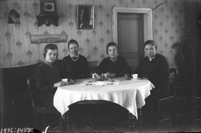 Fyra damer vid kaffebord. Hemmiljö; vardagsrum, soffa.