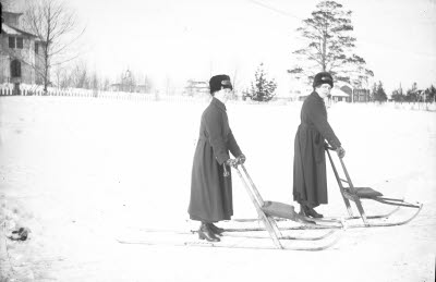 Två slumsystrar med sparkstötting. Gällivare kyrka i bakgrunden.