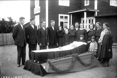 Skjutsstation; bostadshus; gårdsplan. Begravning; svepning: avliden person i öppen kista; gruppbild: anhöriga. Oidentifierade.