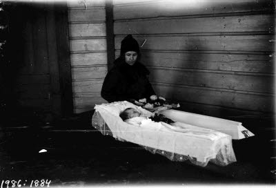 Sörjande mor vid öppen kista med ett barn. Oidentifierade.