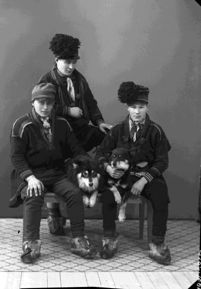 Porträtt av tre herrar i samedräkter och två hundar. Ateljefoto.