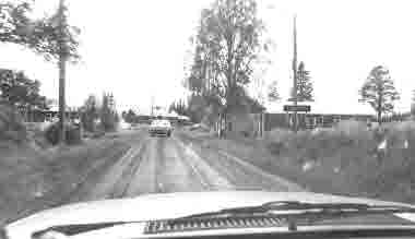 Liviöjärvi, Pajala kommun. Vägskylt; ortnamnsmärke. Grusväg. Bilar. Hus.