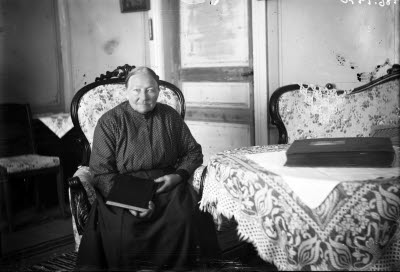 En äldre dam. Hemmiljö; vardagsrum. Högreståndsmiljö.