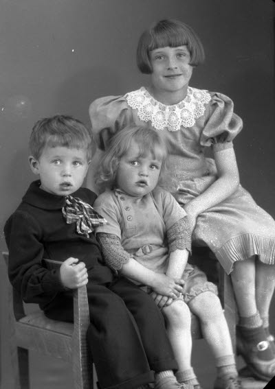 Porträtt av tre barn; två flickor och en pojke. Ateljefoto.