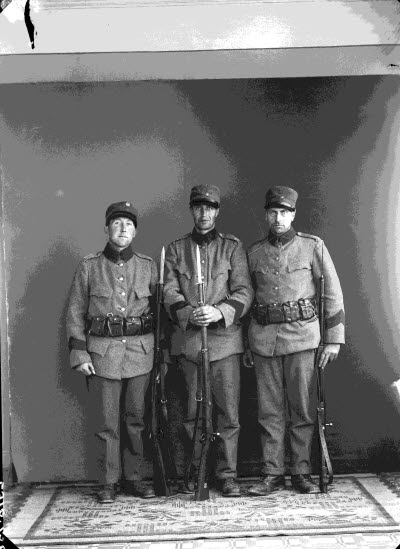 Porträtt av tre herrar, militärer, med gevär. Ateljefoto.