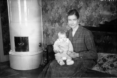 En kvinna och ett barn. Hemmiljö; vardagsrum, kakelugn.