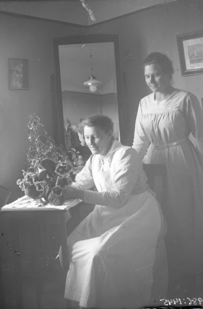 Två damer i hemmiljö. Troligen sjukvårdspersonal.