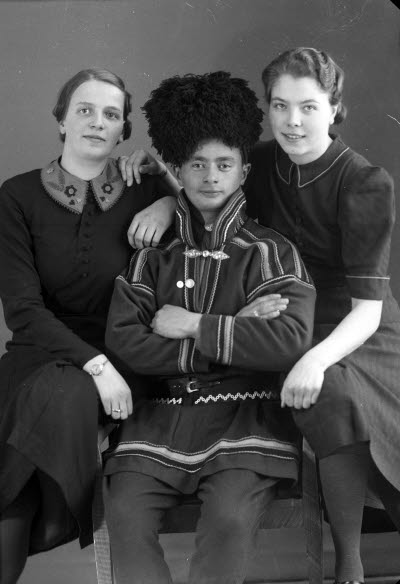 Porträtt av en herre i samedräkt och två damer. Ateljefoto.