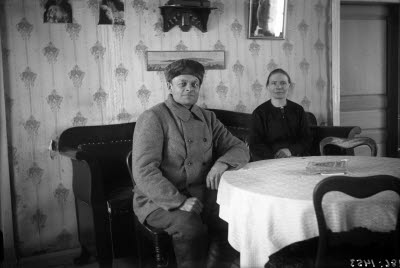 En äldre herre och dam. Hemmiljö; vardagsrum. Soffa.