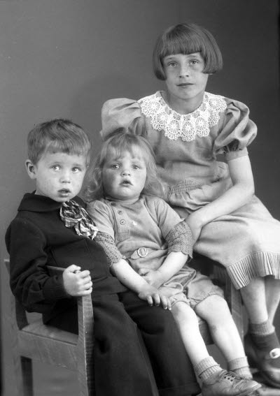 Porträtt av tre barn; två flickor och en pojke. Ateljefoto.