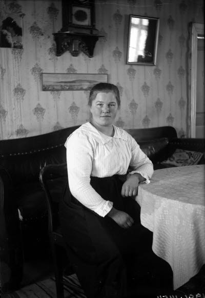 En äldre dam. Hemmiljö; vardagsrum. Soffa.