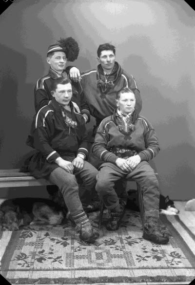 Porträtt av fyra herrar i samedräkter samt hundar. Ateljefoto.