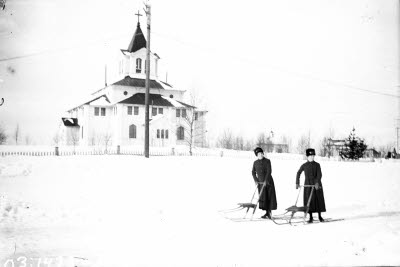 Två slumsystrar med sparkstötting. Gällivare kyrka i bakgrunden.