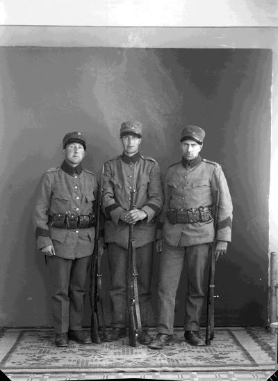 Porträtt av tre herrar, militärer, med gevär. Ateljefoto.