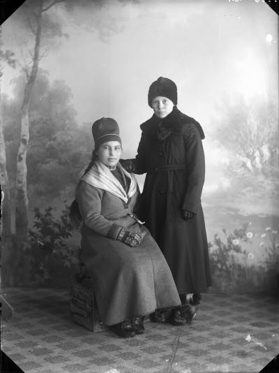 Porträtt av en dam i kappa och en dam i samedräkt. Ateljefoto.