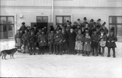 Människor i samedräkter framför hus.