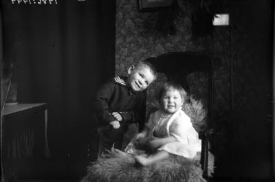 Två barn. Flicka och pojke i hemmiljö. Vardagsrum.