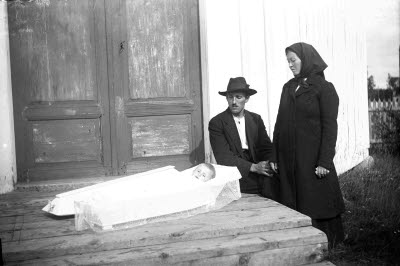 Sörjande föräldrar vid öppen kista med avlidet barn. Oidentifierade. 